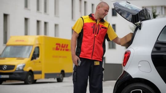 DHL legt Pakete im Kofferraum eines Smart ab