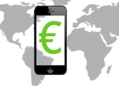 Ein Smartphone zeigt auf dem Display das Euro-Symbol, im Hintergrund ist eine Weltkarte zu sehen.