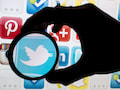 Das Icon des Nachrichtendienstes Twitter ist auf einem Monitor durch eine Linse zu sehen, whrend weitere Icons daneben angeordnet sind.