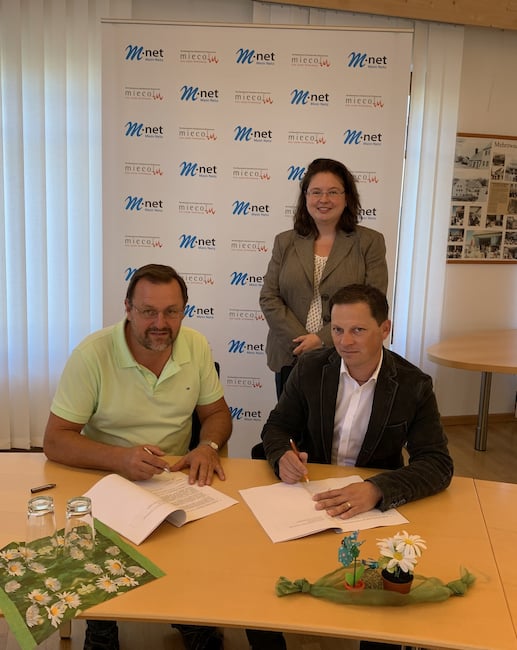 Brgermeister Heinrich Jckle (links) und Tobias Miessl (miecom) unterzeichnen den Ausbauvertrag fr Heretsried. Hinter ihnen Melanie Hundt von M-net.