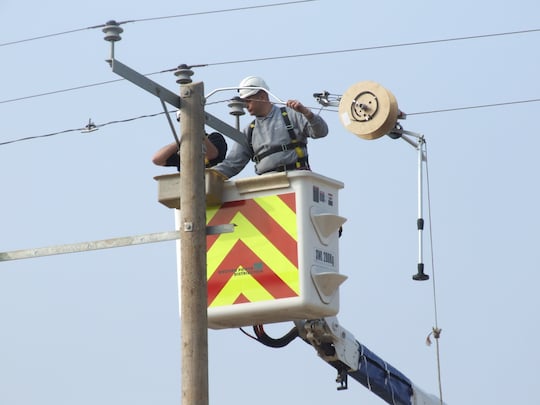 zwei Mnner mit Helmen befestigen an einem Strommast ein Kabel